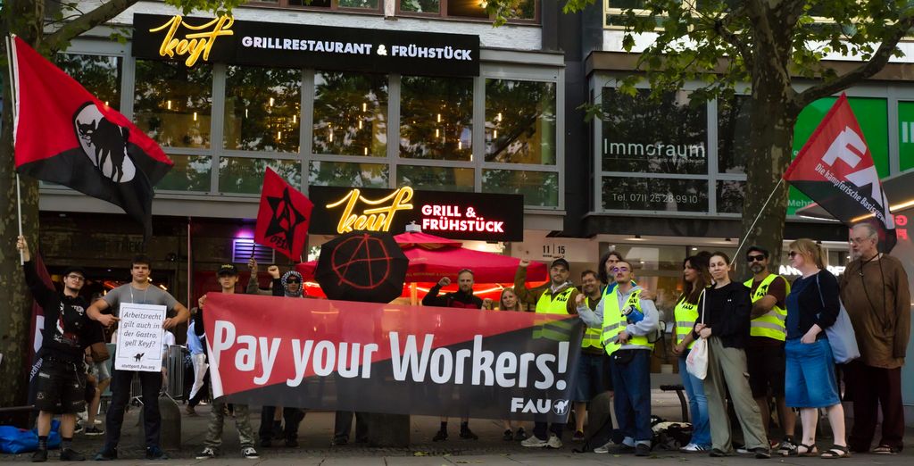 Das Foto zeigt die Solikundgebung vor dem Keyf am 17. Juli 2026 mit solidarischen Teilnemer*innen und dem Pay Your Workers Transpartent
